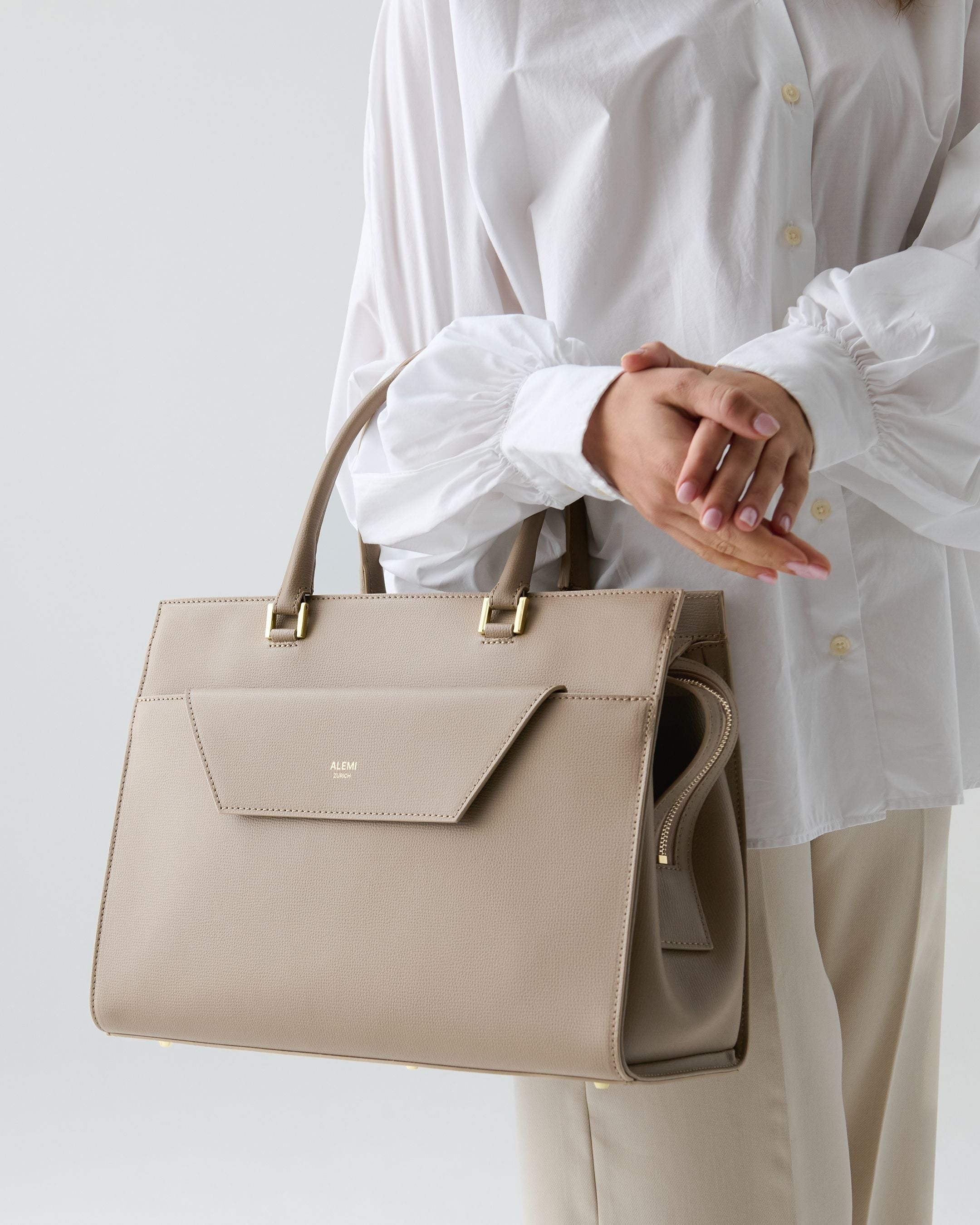 ALEMI Zurich | CENTRAL | Laptop Bag | Greige | Pebbled Leather | Model carrying bag by handle-close-up