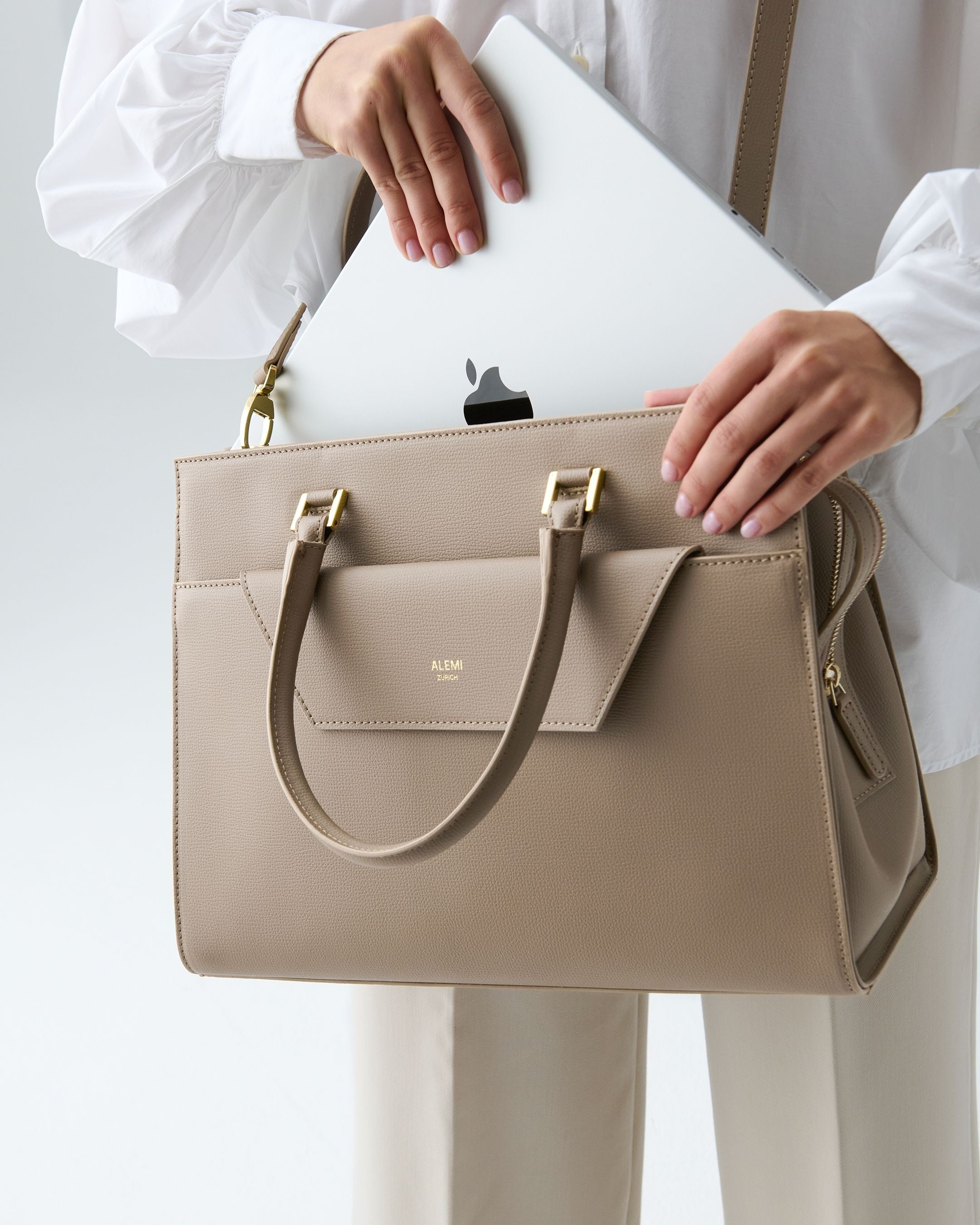 ALEMI Zurich | CENTRAL | Laptop Bag | Greige | Pebbled Leather | Model carrying bag by strap laptop