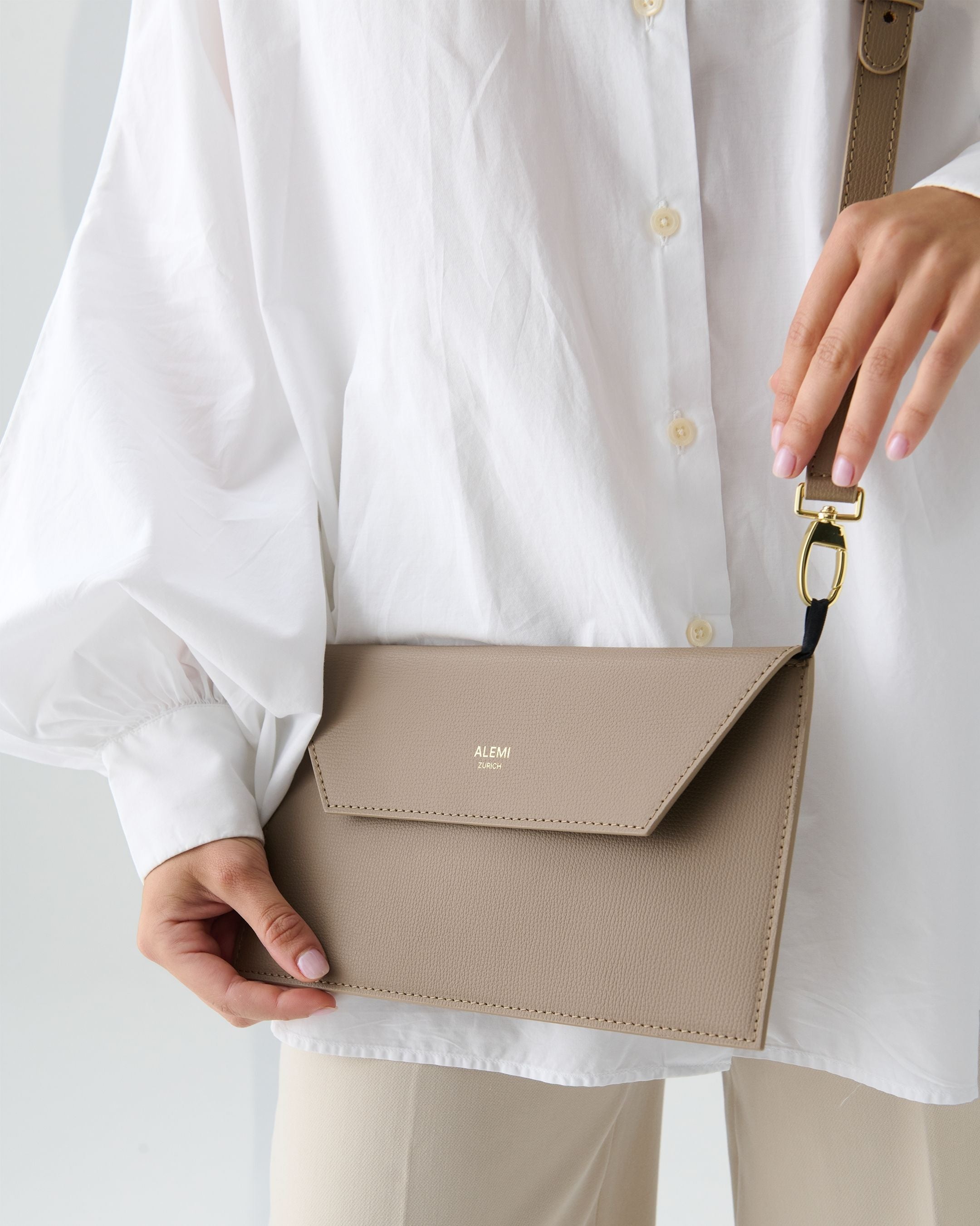 ALEMI Zurich | CENTRAL | Laptop Bag | Greige | Pebbled Leather | Model carrying Clutch by strap