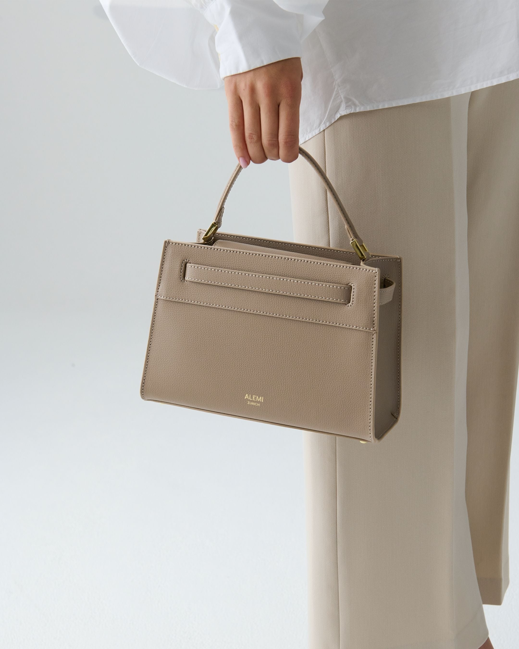 ALEMI Zurich | SEEFELD MINI | Small Bag | Greige | Pebbled Leather | Model carrying bag by handle close up