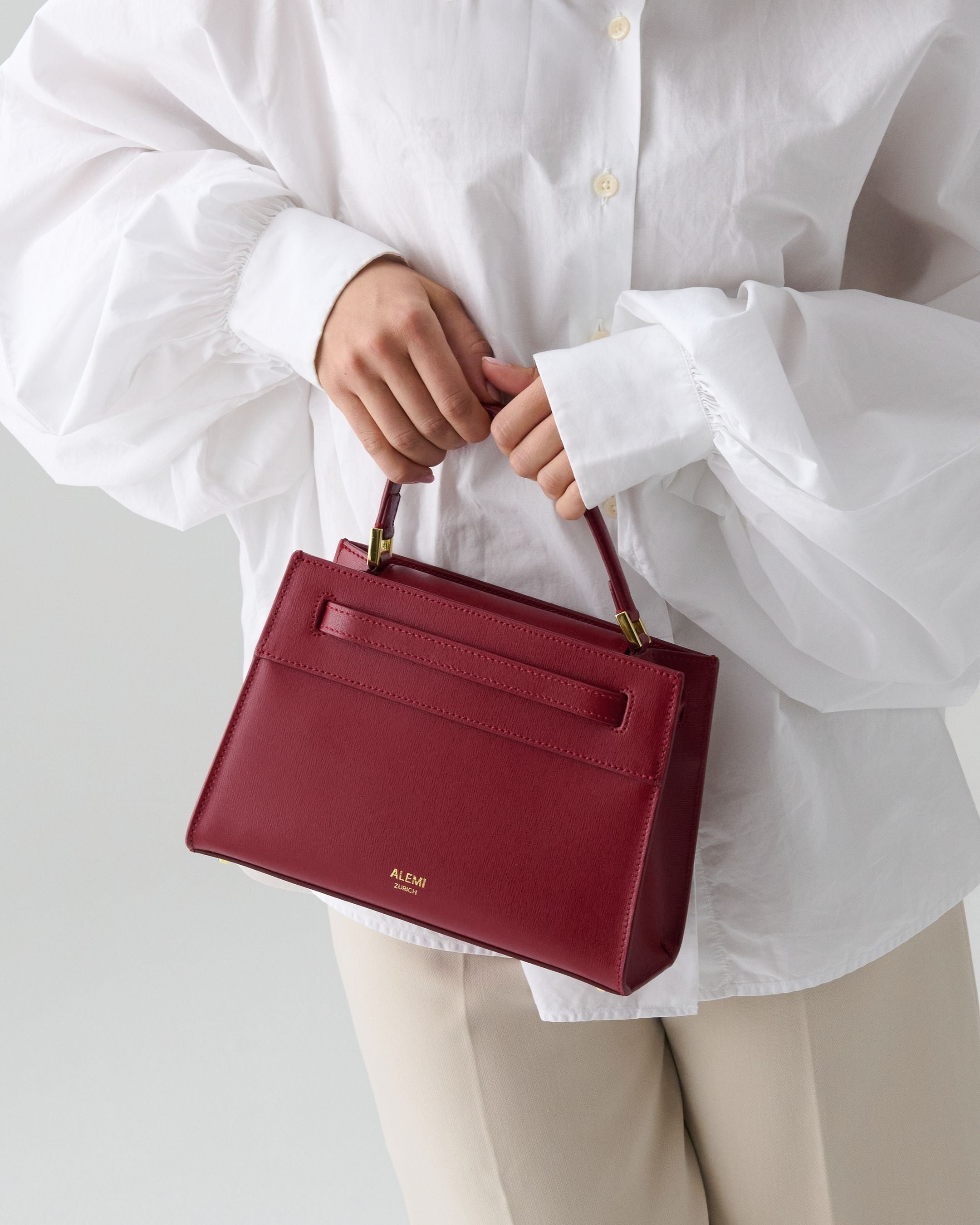 ALEMI Zurich | SEEFELD MINI | Small Bag | Red | Saffiano Leather | Model carrying bag by handle close up